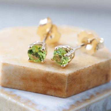 Close-up of 14kt yellow gold peridot stud earrings on a marble surface
