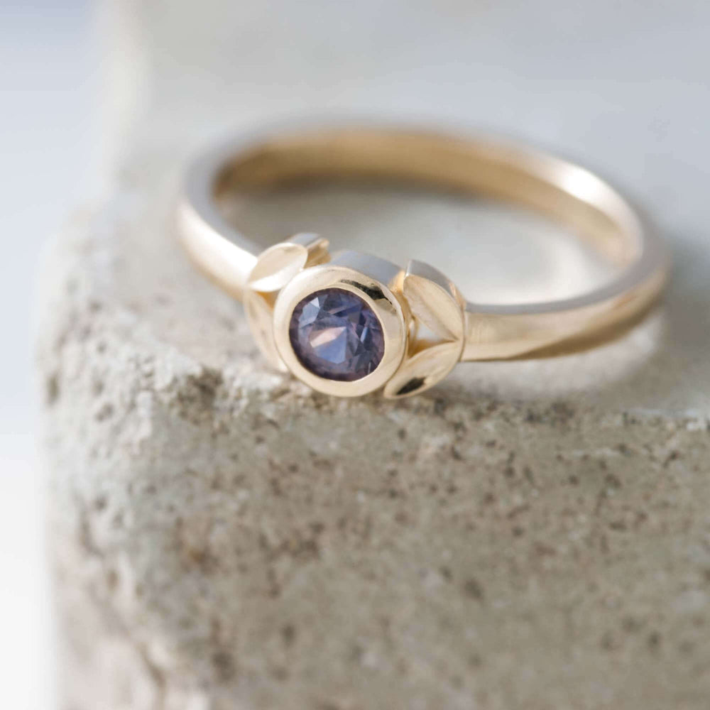 Close-up of 14kt yellow gold ring with bezel-set purple Montana sapphire on stone surface