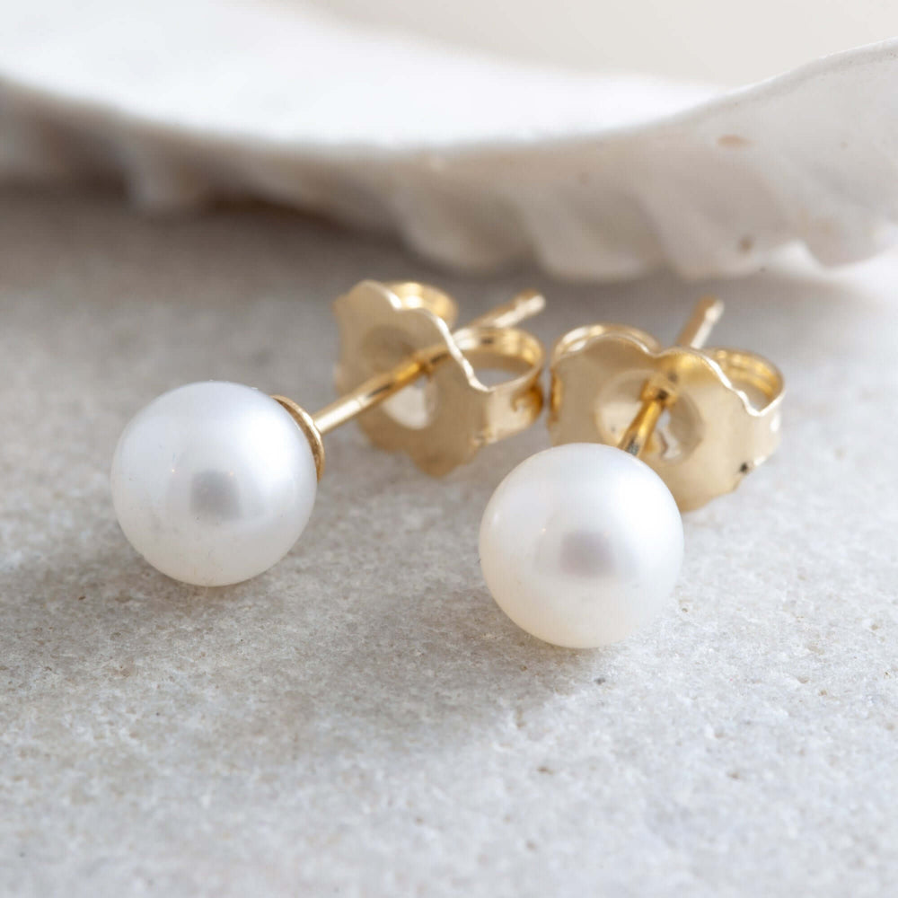 Close-up of 5mm freshwater pearl stud earrings with yellow gold posts and backs