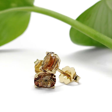 Close-up of 14kt yellow gold andalusite stud earrings with green leaf accent