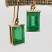 Close-up of vintage emerald and 14kt yellow gold dangle earrings on stand