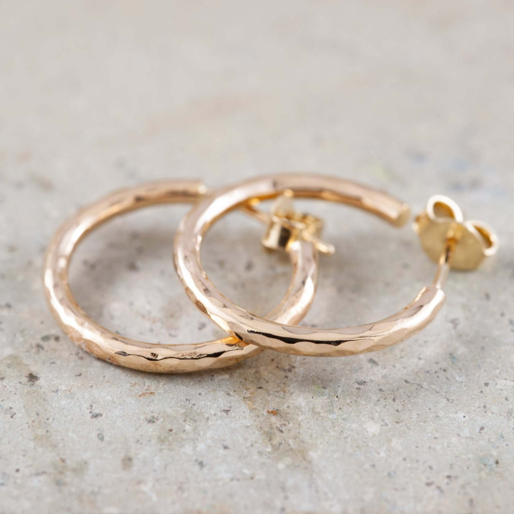 Close-up of hammered 14K yellow gold hoop earrings on a stone surface