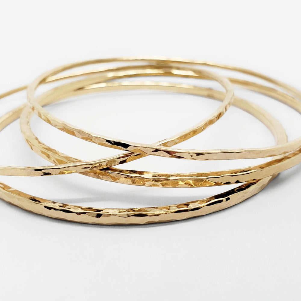 Close-up of stacked hammered 14kt yellow gold bangles on white surface