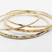 Close-up of stacked hammered 14kt yellow gold bangles on white surface