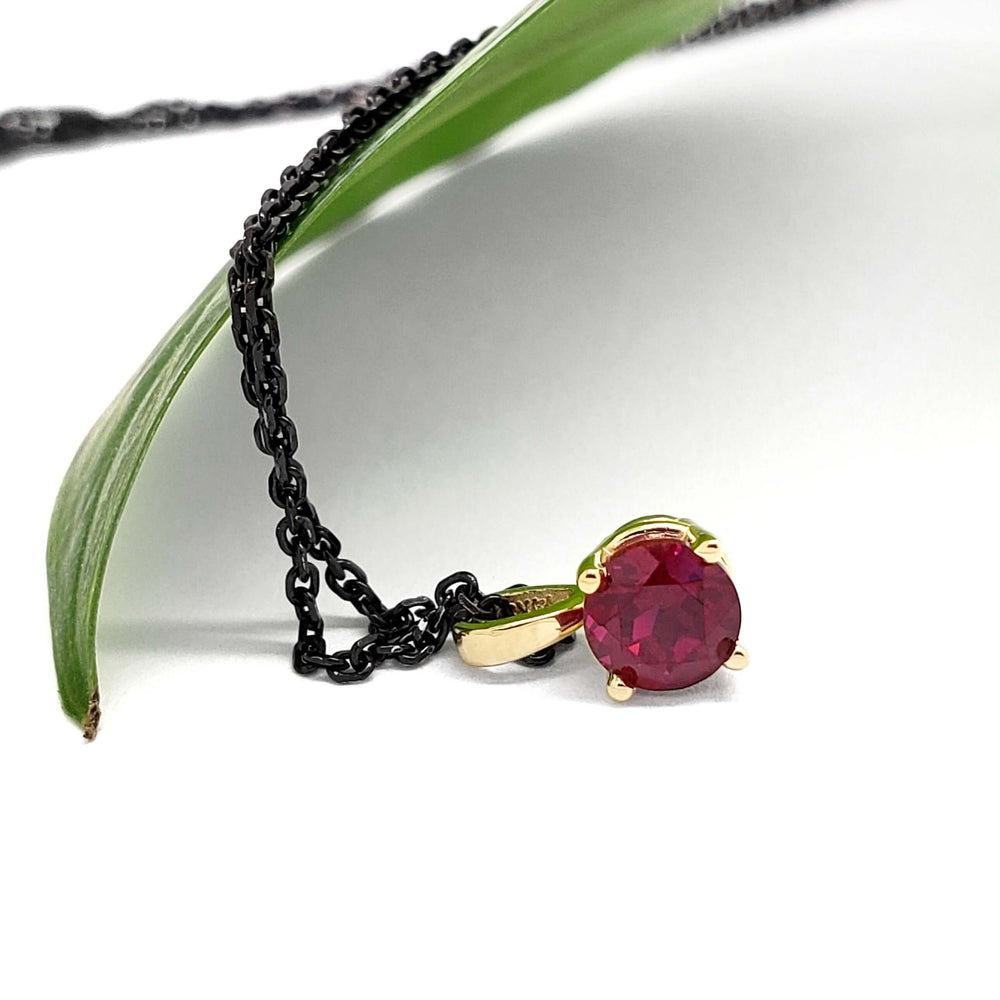 Close-up of 14kt yellow gold lab ruby pendant with black chain and green leaf