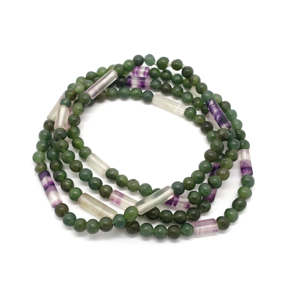 Fluorite and serpentine beaded necklace coiled in a circle on a white background