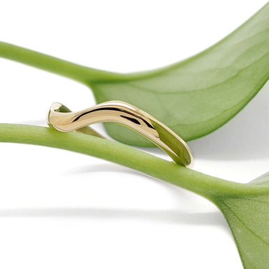 Curved 14kt yellow gold chevron ring resting on a green leaf