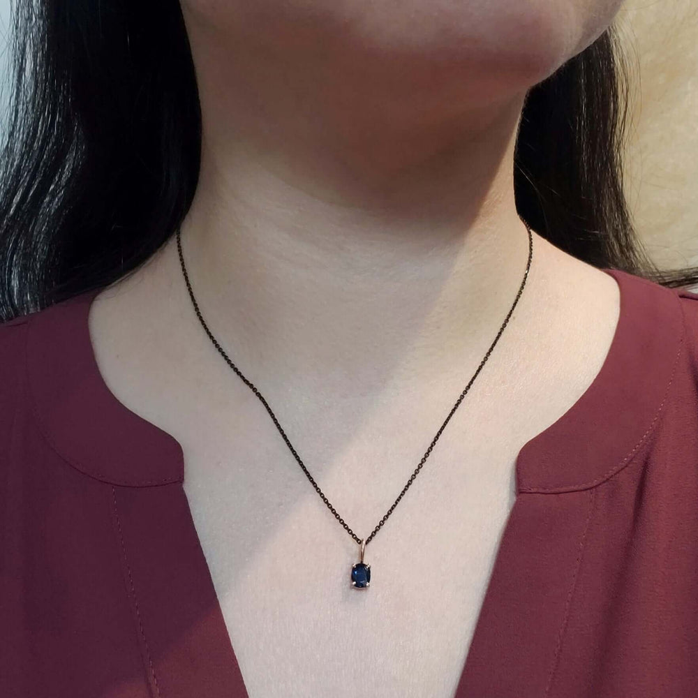 Cushion blue sapphire pendant in yellow gold on a black chain, worn on a woman's neck