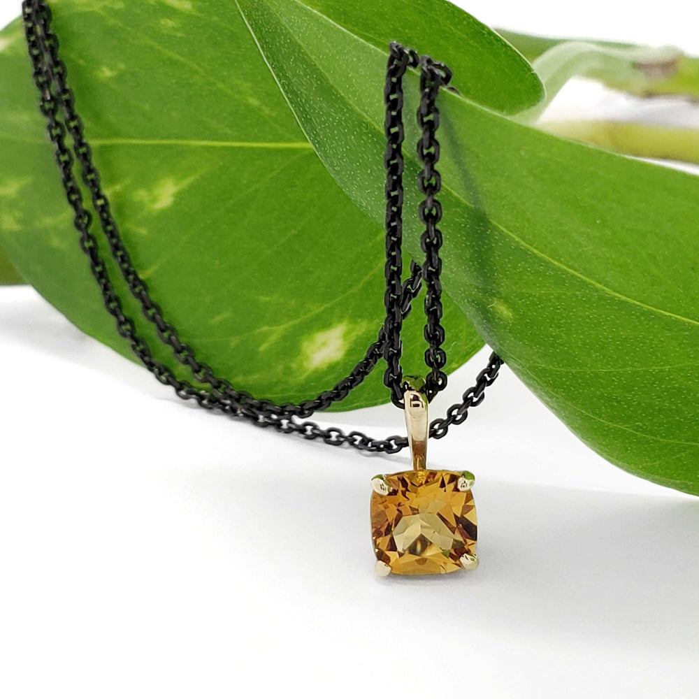 Cushion citrine pendant in yellow gold on black chain, styled on green leaf