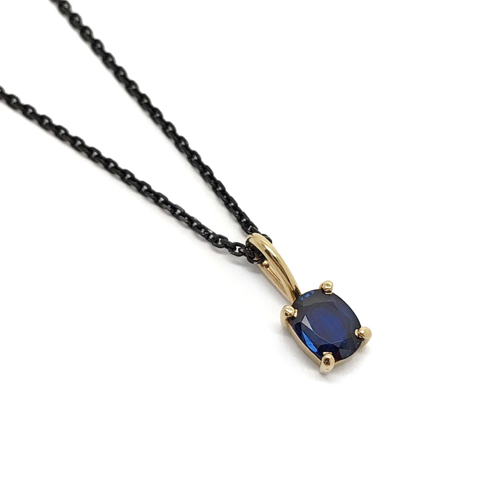 Cushion cut deep blue sapphire pendant in 14kt yellow gold on a black chain, front view