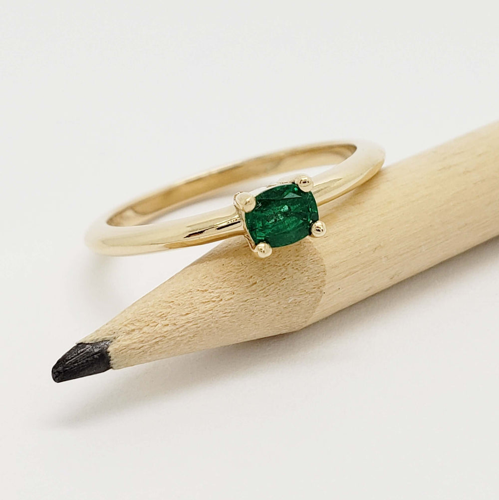 Cushion cut emerald yellow gold ring resting on a pencil