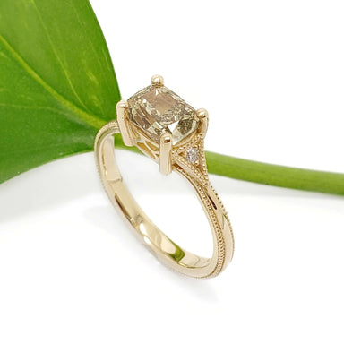 Cushion cut lab diamond engagement ring in yellow gold with pave accents, by a green leaf