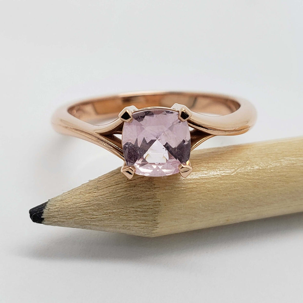 Cushion cut pink sapphire engagement ring in rose gold shown with a pencil for scale