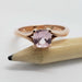 Cushion cut pink sapphire engagement ring in rose gold shown with a pencil for scale