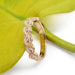 Diamond and rose gold wedding band with millgrain detail on a green leaf