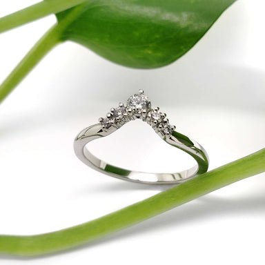 Diamond chevron wedding ring in white gold beside a green leaf