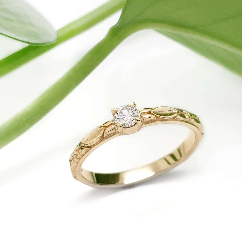Diamond engagement ring in 14kt yellow gold with leaf motif, shown with green leaves