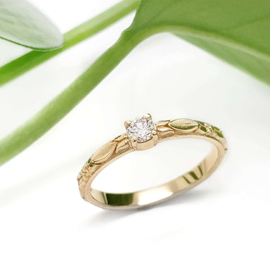 Diamond engagement ring in 14kt yellow gold with leaf motif, shown with green leaves