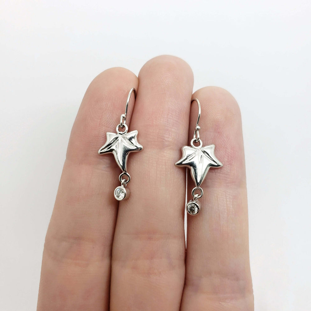 14kt white gold leaf dangle earrings with bezel set diamonds shown on fingers