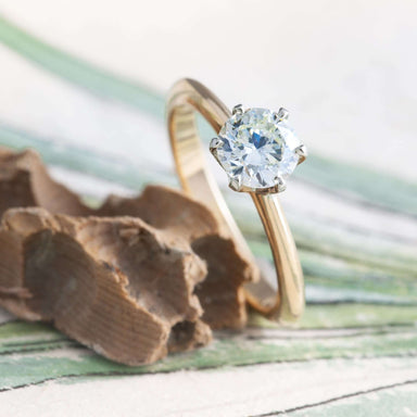 Diamond solitaire engagement ring in two tone gold displayed on textured background