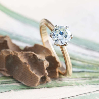 Diamond solitaire engagement ring in yellow and white gold, displayed on textured background