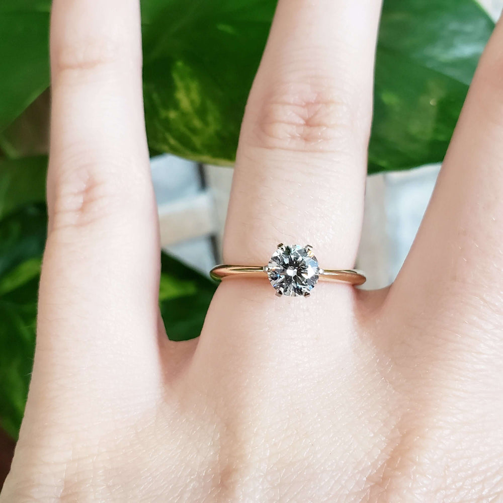 Diamond solitaire ring in yellow and white gold, worn on hand with leafy background