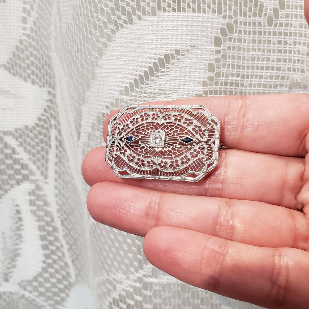 Edwardian filigree brooch with sapphires shown in hand for size scale