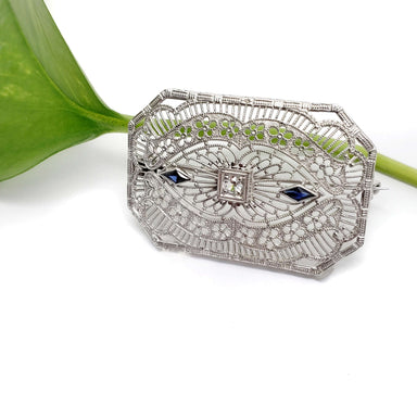 White gold Edwardian brooch with blue synthetic sapphires, displayed against a leaf