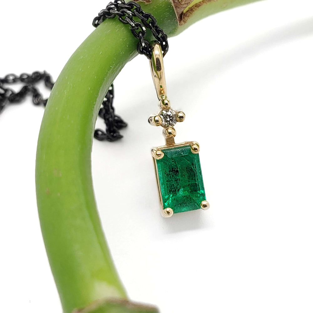 Emerald and diamond 14kt yellow gold pendant displayed on a green stem