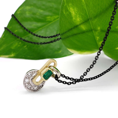 Emerald and diamond vintage pendant in 18kt gold, shown on black chain with green leaf background