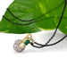 Emerald and diamond vintage pendant in 18kt gold, shown on black chain with green leaf background