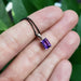 Emerald cut amethyst pendant in 14kt white gold with black chain shown on a hand