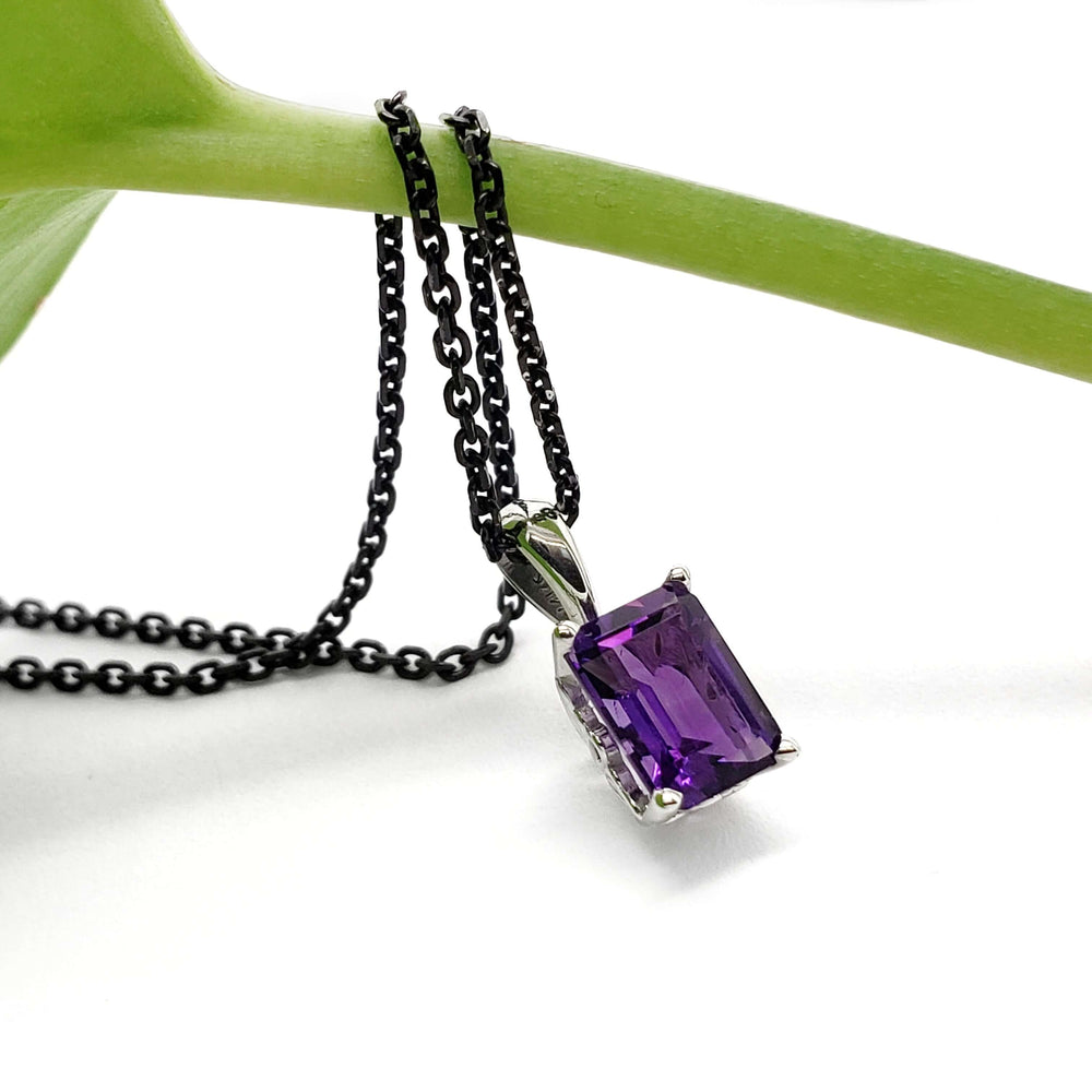 Emerald cut amethyst pendant in 14kt white gold with black chain draped on a green stem