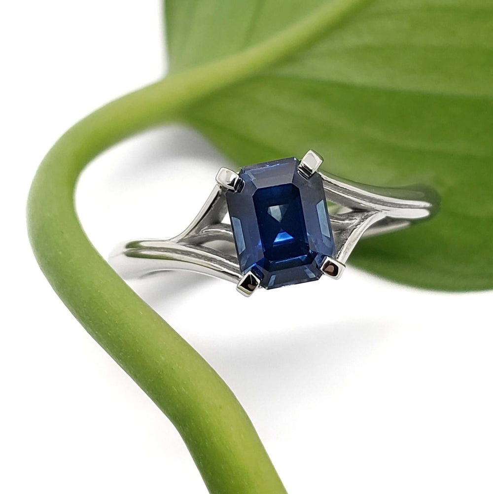 Emerald cut blue Montana sapphire engagement ring in white gold, with leaf background