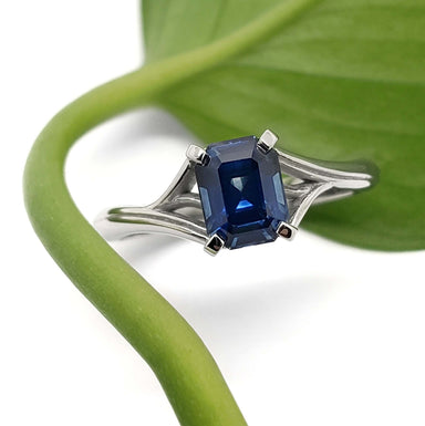 Emerald cut blue Montana sapphire engagement ring in white gold, with leaf background