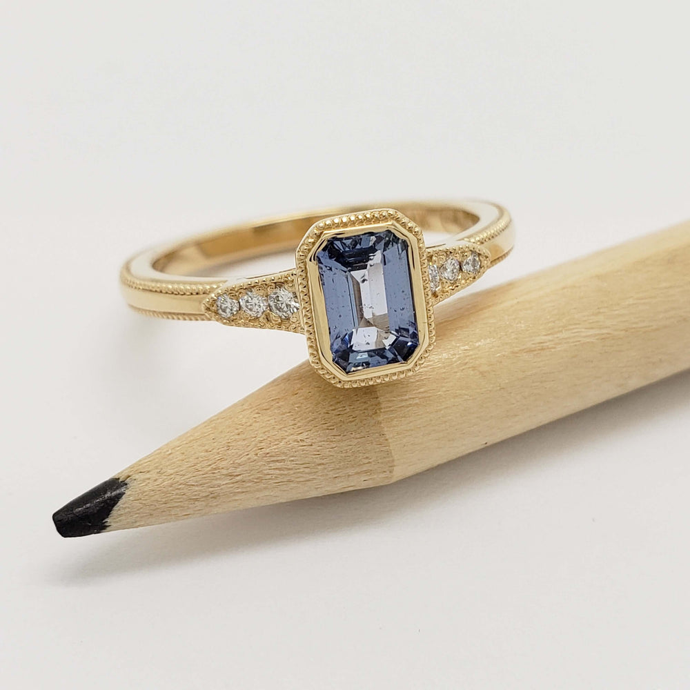 Emerald cut blue sapphire and diamond engagement ring in yellow gold, beside pencil