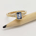 Emerald cut blue sapphire and diamond engagement ring in yellow gold, beside pencil