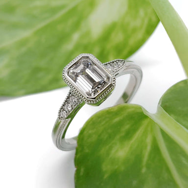 Emerald cut lab diamond engagement ring in 14kt white gold with side diamonds, shown on green leaves