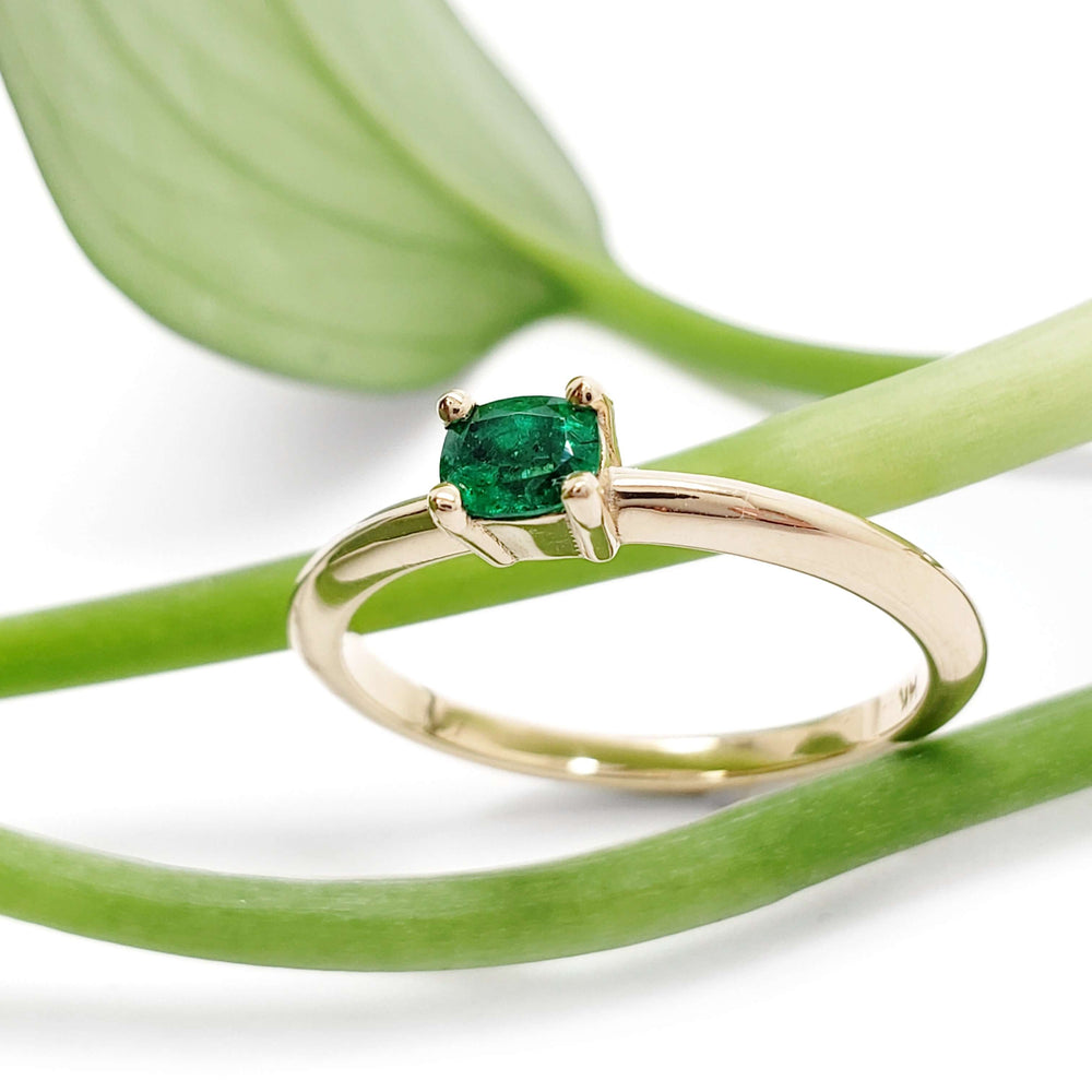 Emerald engagement ring in yellow gold displayed on green leaves