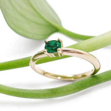 Emerald engagement ring in yellow gold displayed on green leaves
