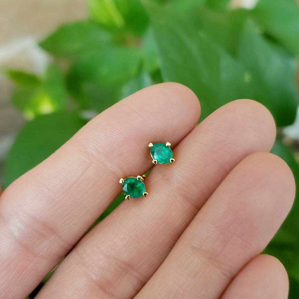 Emerald stud earrings in 14kt yellow gold with heart prongs, displayed on fingertips