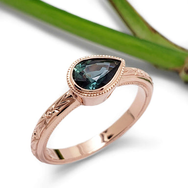 Engraved 14kt rose gold ring with pear teal sapphire, shown with green leaf