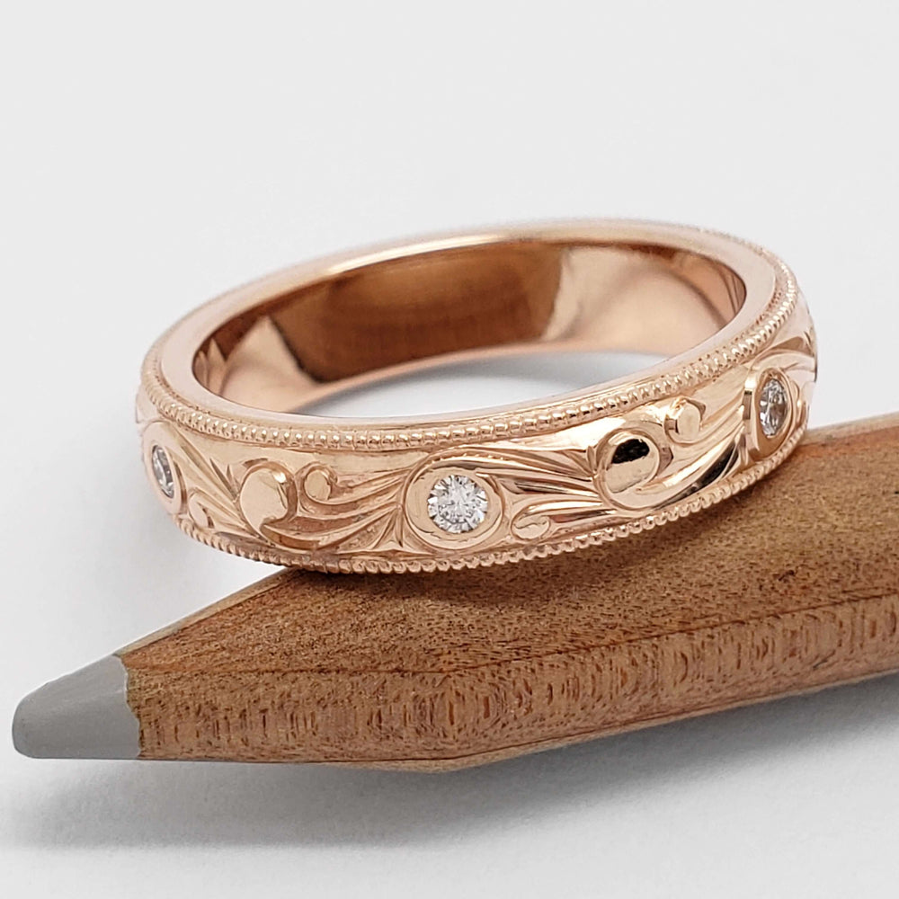 Engraved 14kt rose gold wedding ring with Canadian diamonds, resting on a pencil