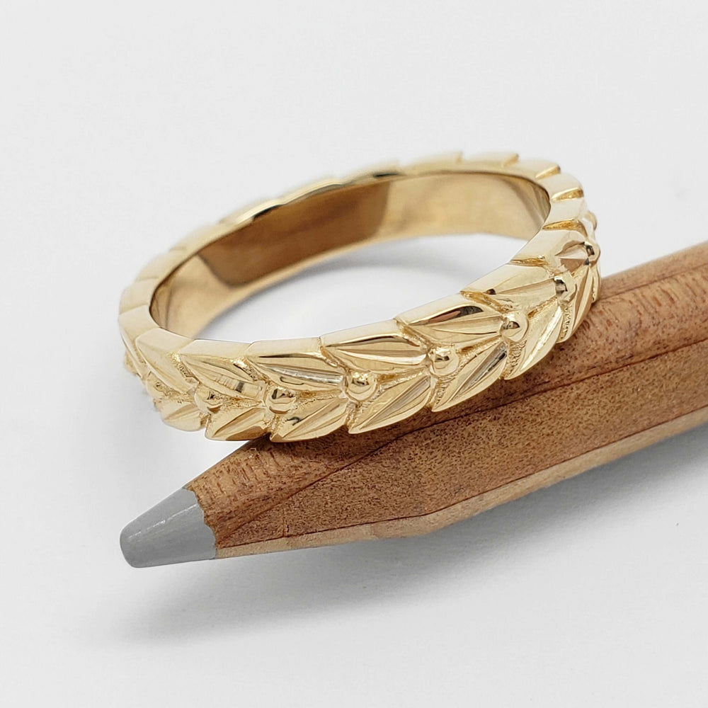 Engraved 14kt yellow gold leafy wedding ring resting on a wooden pencil