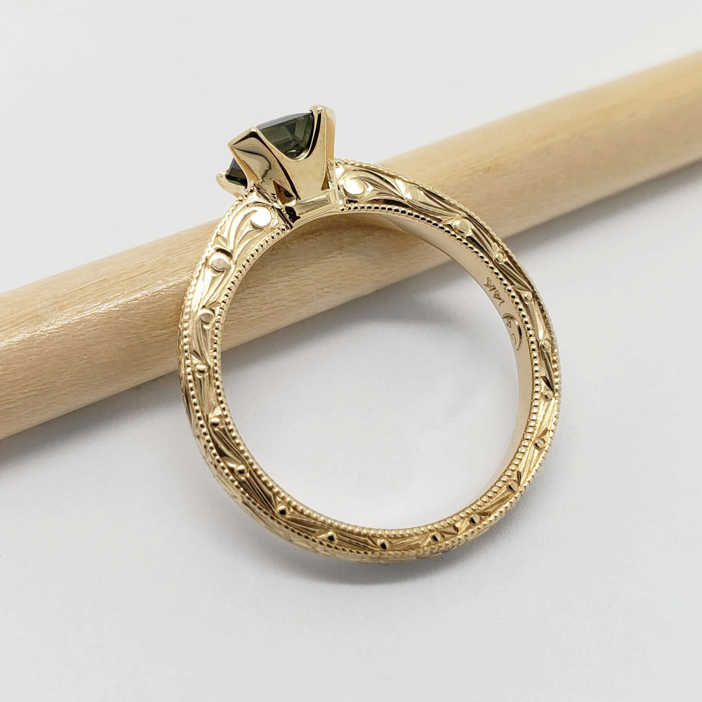Side view of engraved 14kt yellow gold ring with teal Australian sapphire, showing detailed hand engraving