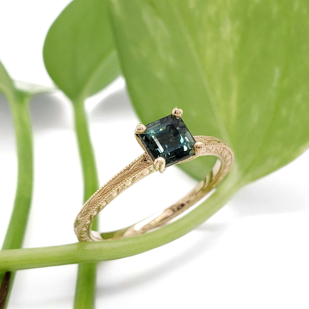 Engraved 14kt yellow gold ring with green asscher cut sapphire, shown with greenery