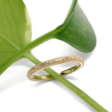 Engraved 14kt yellow gold wedding ring displayed on a green leaf