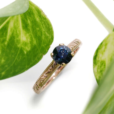 Engraved 14kt rose gold ring with blue Australian sapphire, shown with green leaves