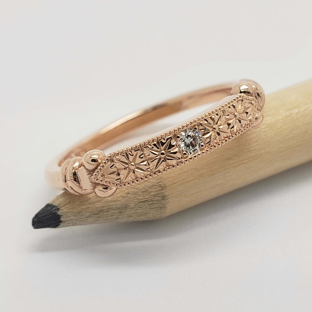 Engraved rose gold wedding ring with lab diamond, displayed on a pencil