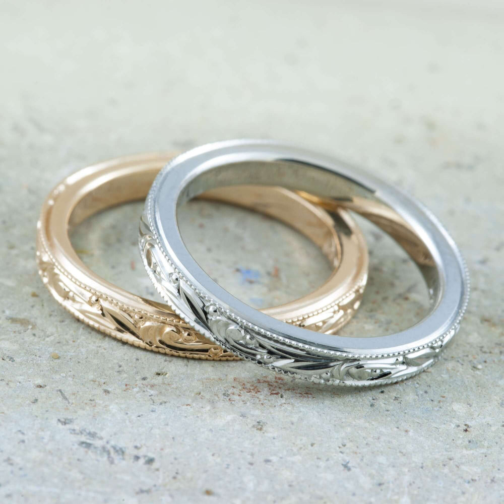 Engraved wedding rings in 14k white gold and rose gold on a stone surface